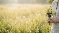 Woman in white linen dress holding wildflower bouquet in sunny meadow field, spring nature background for lifestyle and wedding themes.