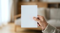 Person holding blank white paper sheet in modern home interior, mockup for branding, marketing materials, or promotional content display.