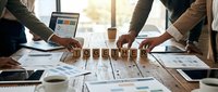 Business team collaborating over wooden letter blocks spelling TOGETHER on conference table with laptops, documents and coffee in modern office.