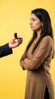Young woman rejecting marriage proposal with engagement ring on yellow background, relationship conflict and breakup concept.