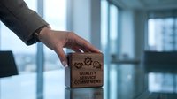 Professional businessman hand selecting wooden block with quality service commitment icons in modern office environment for business excellence concepts.