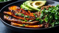 Grilled sweet potato slices with fresh herbs and avocado on dark plate. Healthy vegetarian meal with caramelized edges and vibrant colors for nutrition content.