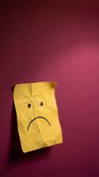 Yellow crumpled paper bag with sad face drawn on burgundy wall expressing disappointment, depression, mental health awareness concept for therapy materials.