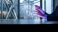 Businesswoman in dark suit with purple gloved hand interacting with digital holographic interface displaying data visualization on modern office desk with city skyline background.