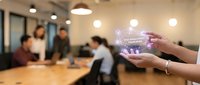Hands holding a glowing holographic risk management framework display in a modern office with colleagues meeting in the background.