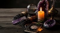 Mystical fortune telling setup with tarot cards, burning candle, amethyst crystals, and dried herbs on rustic wooden table for spiritual guidance sessions.