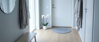 Bright Scandinavian entryway with round welcome mat, white orchid, wooden bench, and hanging robes on hooks near a front door.