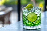 Fresh green cocktail with lime slices and ice cubes in crystal glass on marble table, selective focus with blurred background for bar menu.