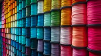Colorful rows of thread spools arranged on shelves creating vibrant rainbow pattern, perfect for sewing, crafting and textile industry backgrounds. Macro photography of multicolored threads.