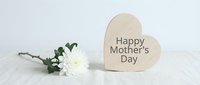 Wooden heart decoration with Happy Mother's Day text and white flowers on marble surface for greeting cards and holiday celebrations.