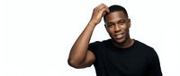 Young African American man wearing black t-shirt, hand raised to head in casual, confident pose against white background for portrait and lifestyle use.