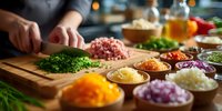 Chef chopping fresh herbs on wooden cutting board with colorful diced vegetables in small bowls ready for cooking preparation.