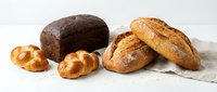 Assorted fresh baked bread loaves and rolls arranged on white surface, including dark rye, crusty baguettes and golden pastries for bakery, food and culinary use.