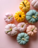 Colorful decorative pumpkins in pastel pink, yellow and mint green shades arranged on soft pink background, creating modern autumn seasonal composition.
