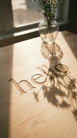 Hello engraved on a light wooden surface with warm sunlight and flower vase shadows creating a cozy, welcoming atmosphere.