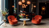Luxurious lounge area with burnt orange velvet armchairs, round marble table, pendant copper lights and floral arrangements creating modern elegant atmosphere.