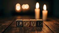 Wooden letter blocks spelling LOVE on rustic table with glowing candles in soft bokeh background, romantic Valentine atmosphere.