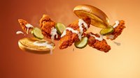 Crispy fried chicken sandwiches with pickles and sauce suspended in mid-air against warm orange background for food advertising and restaurant marketing.