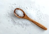 Sea salt crystals on wooden spoon against white background, culinary ingredient for gourmet cooking and food preservation.