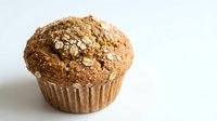 Freshly baked muffin with cinnamon streusel topping in paper wrapper, ideal for bakery, food, and culinary content.