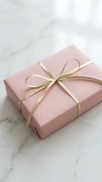 Pink gift box tied with a gold ribbon bow on a marble surface, elegant present for birthday, wedding, or Valentine's Day celebration.