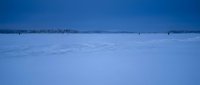 Vast frozen lake covered in pristine white snow under clear blue winter sky with distant forest treeline creating serene arctic landscape for nature backgrounds.