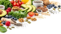 Healthy superfood ingredients including avocado, berries, nuts, seeds and fresh vegetables arranged on white background for clean eating and nutrition.