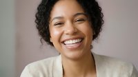 Happy young African American businesswoman with curly hair smiling warmly in beige blazer, professional portrait for corporate and career content.