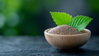 Organic chia seeds in wooden bowl with fresh green mint leaves on dark stone background, healthy superfood concept with copy space for text.
