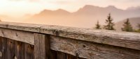 Weathered wooden railing with mountain landscape and misty peaks in soft morning light, suitable for travel and nature backgrounds.