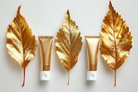 Golden autumn leaves alternating with luxury cosmetic cream tubes on white background, minimal beauty product flatlay composition for skincare branding.