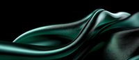 Luxurious emerald green silk fabric with smooth waves and folds against dark background creates dramatic contrast and flowing movement. Suitable for fashion and luxury designs.