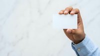 Male hand with medium skin tone holding blank white card against marble background, suitable for business presentations, marketing mockups, and corporate branding designs.