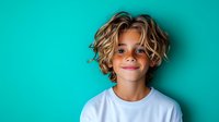 Young boy with wavy blonde surfer hair and bright smile wearing white t-shirt against turquoise background, expressing joy and confidence in casual studio portrait.