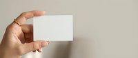Hand holding blank white business card mockup against neutral beige background for branding and corporate identity design projects.
