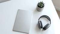 Minimalist workspace with silver tablet, wireless headphones and small succulent plant on clean white desk for modern office productivity and remote work.