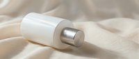 White cosmetic bottle with silver cap on soft beige fabric, luxury skincare product mockup for branding, beauty packaging presentation.