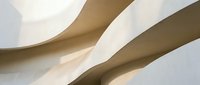Modern architectural interior with flowing curved walls and soft natural lighting creating elegant shadows and geometric patterns in neutral tones.