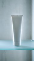 White cosmetic tube on glass shelf with soft lighting for skincare and beauty product packaging mockup design.