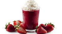 Fresh strawberry smoothie topped with whipped cream in clear glass, surrounded by ripe whole and sliced strawberries on white background. Refreshing summer drink.