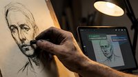 Artist hand sketching detailed portrait drawing with digital tablet reference under warm desk lamp lighting for creative artwork process.