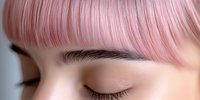 Close up view of pink dyed hair with straight bangs and natural eyebrows on young Asian woman with closed eyes showing modern hair coloring trends.