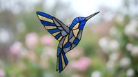 Stained glass hummingbird with blue and yellow wings against blurred spring garden background. Decorative art piece for home decor and nature themes.