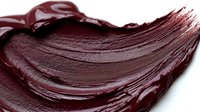 Smooth dark chocolate smear with glossy texture and curved swirl pattern on white background, isolated cosmetic or food product sample for packaging design.