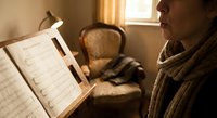Young woman reading sheet music on wooden stand in warm sunlit room with vintage armchair. Classical music practice session at home piano lesson.