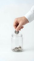 Hand of a Caucasian male professional in white business shirt dropping coin into glass jar filled with coins. Savings, investment, and financial growth concept.