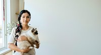 Young South Asian woman holding fluffy cat by window with natural light, suitable for pet care, lifestyle, and animal companionship content.