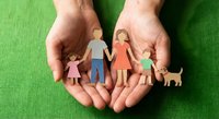 Protective hands holding paper cut family figures with parents, children and pet dog on green fabric background representing care and security.