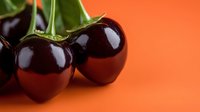 Fresh ripe dark red cherries with green stems on vibrant orange background, healthy organic fruit for summer recipes and natural food photography.