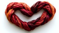 Red and orange wool yarn twisted into heart shape on white background, macro shot showing detailed texture of natural fibers. For crafting, valentine designs and love concepts.